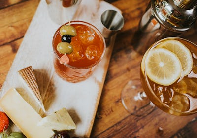 Top down image of a wooden cheese board / platter on a rustic wooden table. It includes various type...