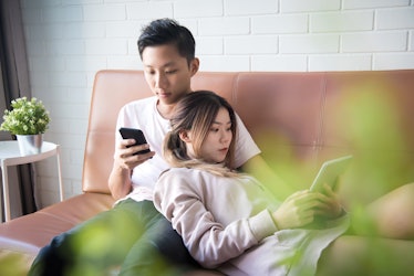 Lovely Asian couple enjoy surfing net and text messaging together while feeling cozy and laziness on...