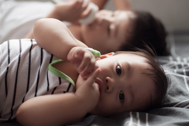Waist-up candid portrait of Southeast Asian baby boy siblings drinking milk together while lying dow...