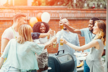 Pregnant woman drinking non-alcoholic beer. Side view of people standing and drinking near barbecue....