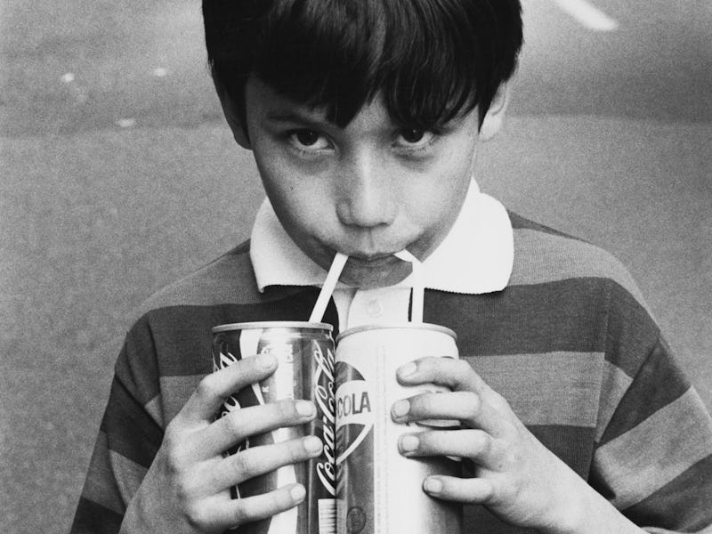 A little boy drinks a can of Coca-Cola and a can of Pepsi-Cola simultaneously in New York City, USA,...