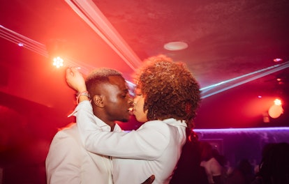Side view of young African American man and woman hugging and kissing while dancing in red light dur...
