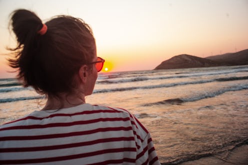 A woman is on the beach, she is looking at the sea and sunset