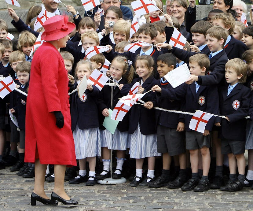 British school children dressed in uniform of blue dresses, gray shorts, and dark blazer greet Queen...