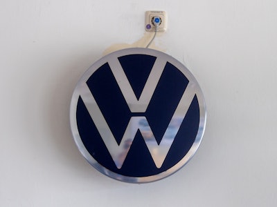 23 June 2021, Saxony, Zwickau: A plug leads from a VW logo to a socket in a conference room at the V...