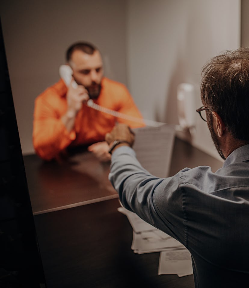 Two men, male prisoner talking over the phone with his lawyer in prison visit room.