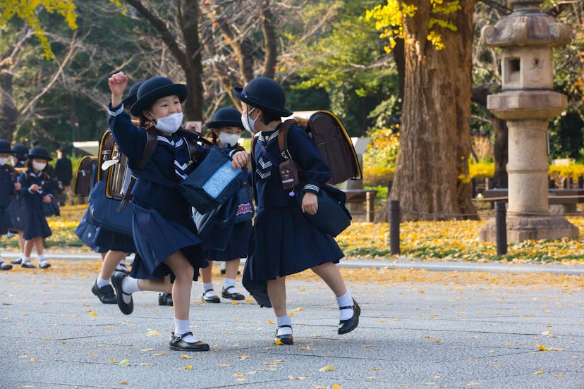 Japanese elementary school girls students dressed in traditional uniforms while wearing face masks w...