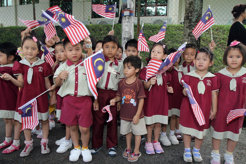 Schoolchildren wave Malaysia flags wearing red and white school uniforms