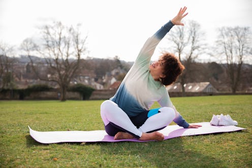A person wears a sweater while doing yoga on a mat in a park. Working out while you're sore can help...