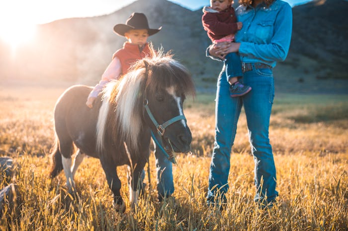 Western female rancher walking with brother and baby sister and pony through sunny Utah grassland.