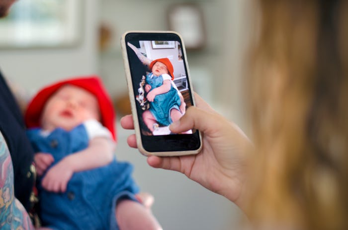 A parent snaps a photo of a newborn baby on a cellphone amid news Apple is rolling out a new feature...