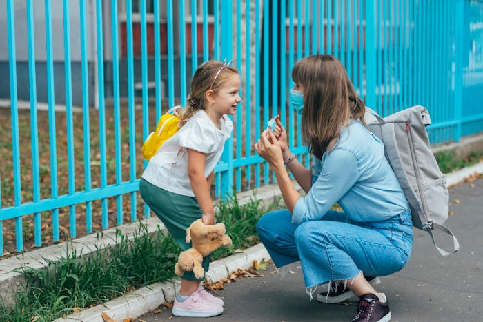 A caring mother helping her daughter put on her face mask before school