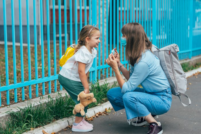 A caring mother helping her daughter put on her face mask before school