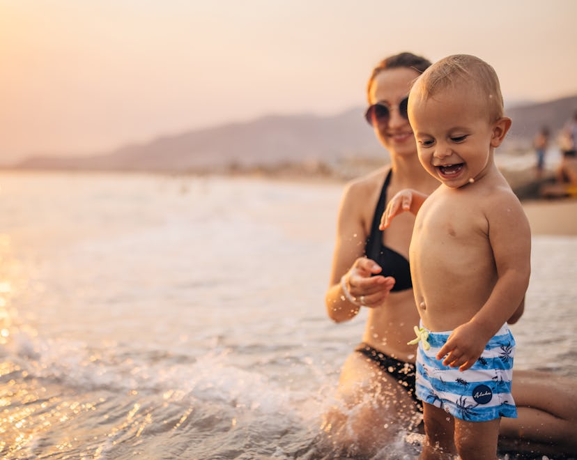 Mother with her little boy son on vacation, they are having fun on the beach in sunset.