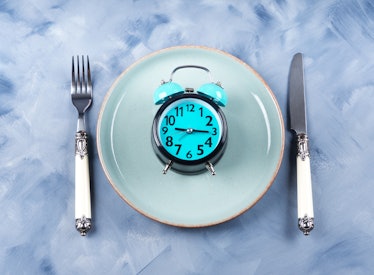 Intermittent fasting concept with blue alarm clock on empty dish with silverware
