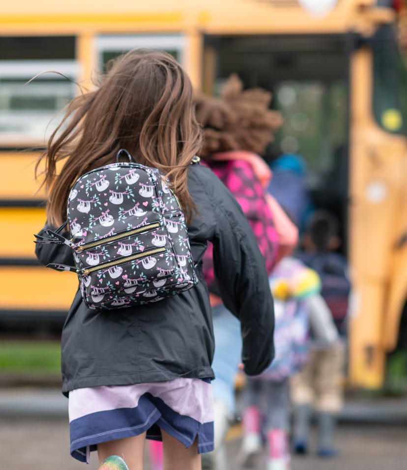 Kids run onto the school bus wearing their jackets and backpacks.