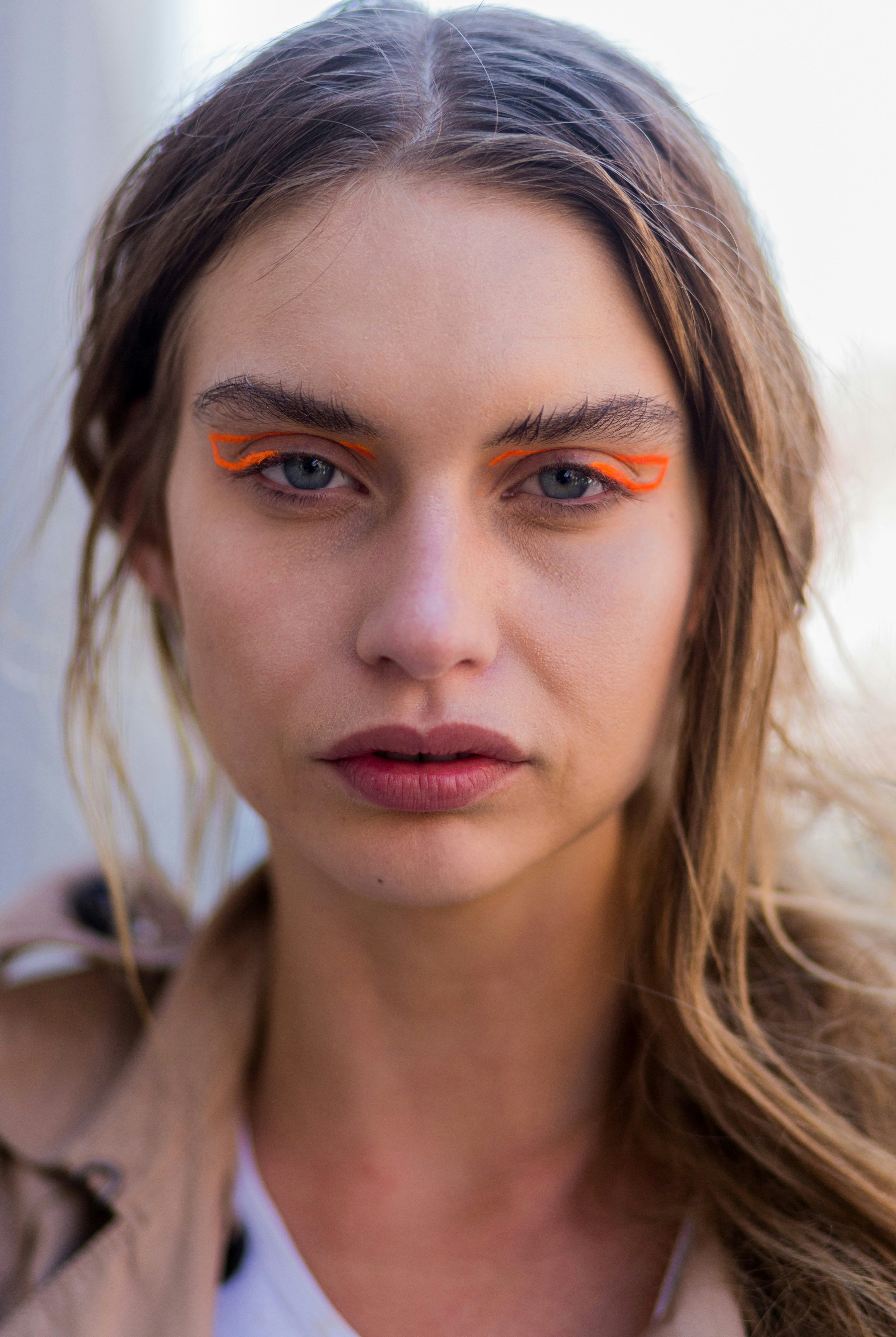 A white young model demonstrates how to wear bright orange graphic eyeliner