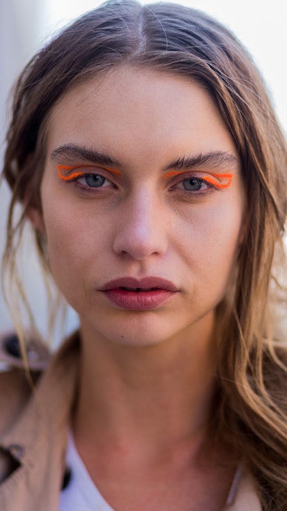 A white young model demonstrates how to wear bright orange graphic eyeliner