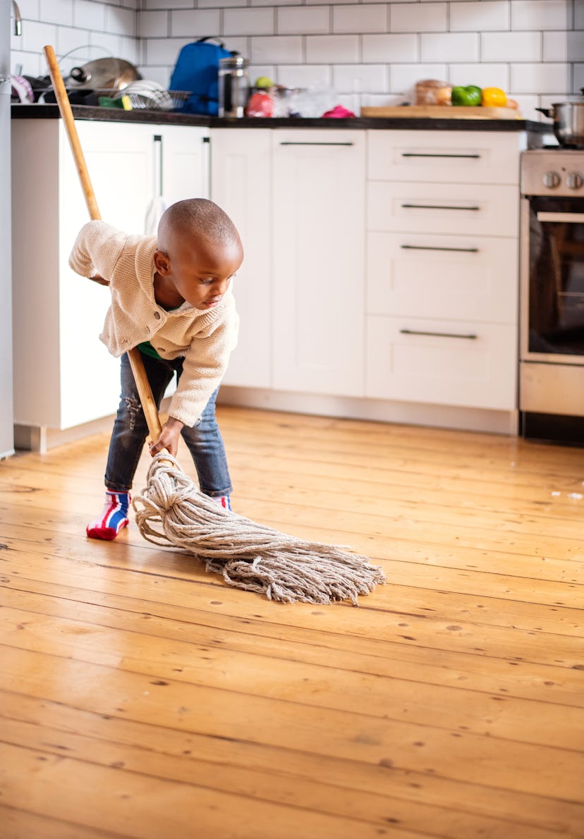 Cute little African boy trying to help around the house by cleaning the kitchen floors with a mop