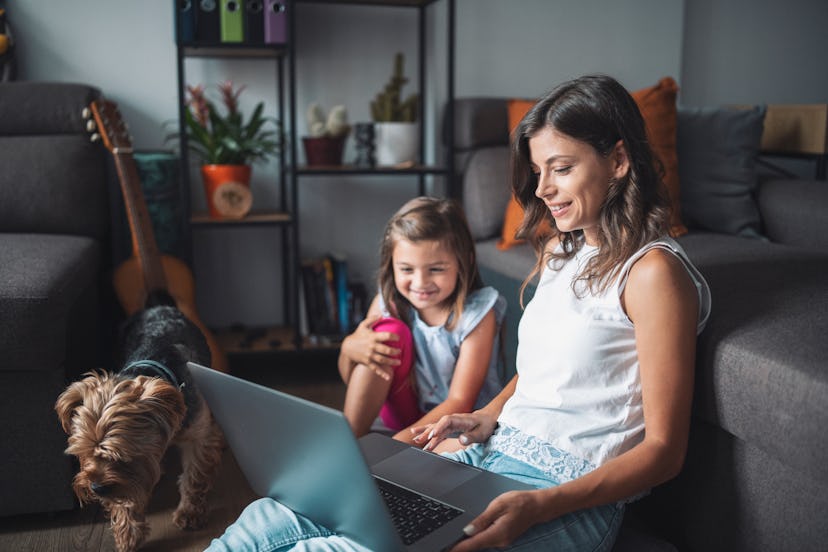 Shot of a young mother and little girl using a laptop and having fun together with their dog next to...