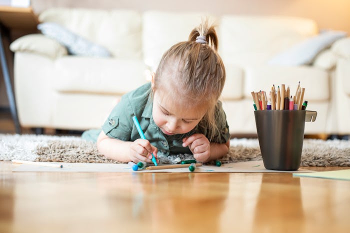 Little girl laying on living room floor, coloring and drawing.