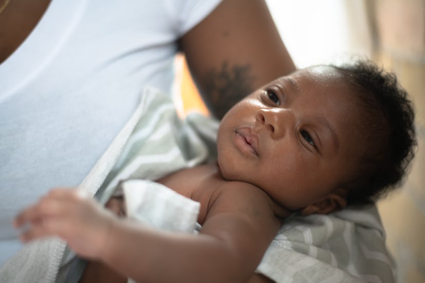 A young African infant baby boy is cradled in his mothers arms as he lays contently awake.  He is sw...