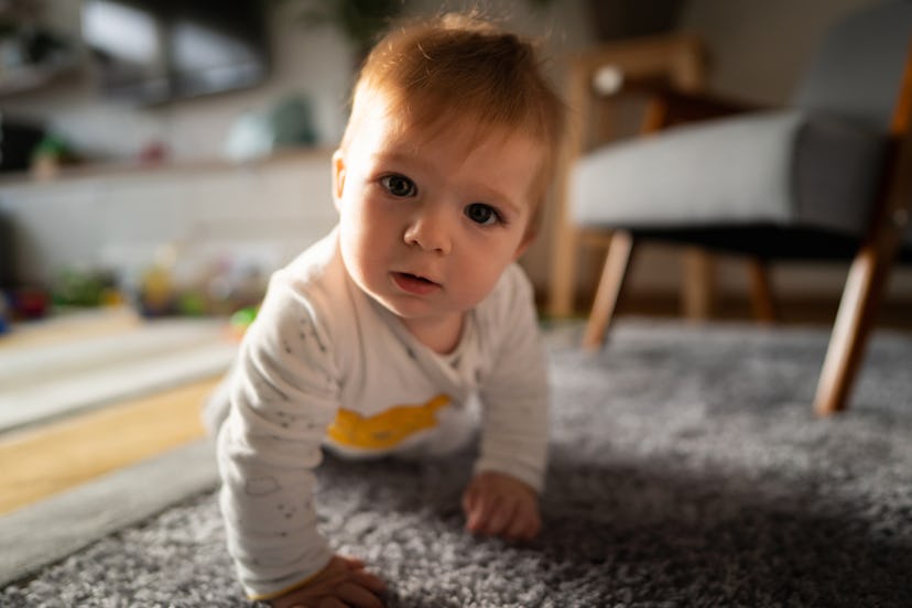 Portrait of a Caucasian baby boy crawling on the floor and looking at the camera.