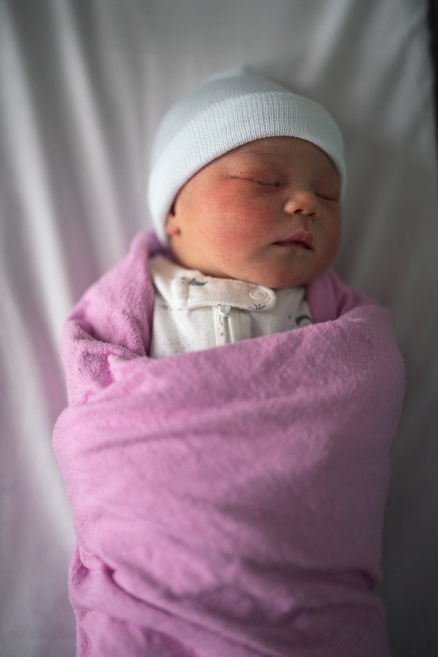 A mixed race Asian newborn is swaddled and laying in a bassinet at the hospital. The child is only a...