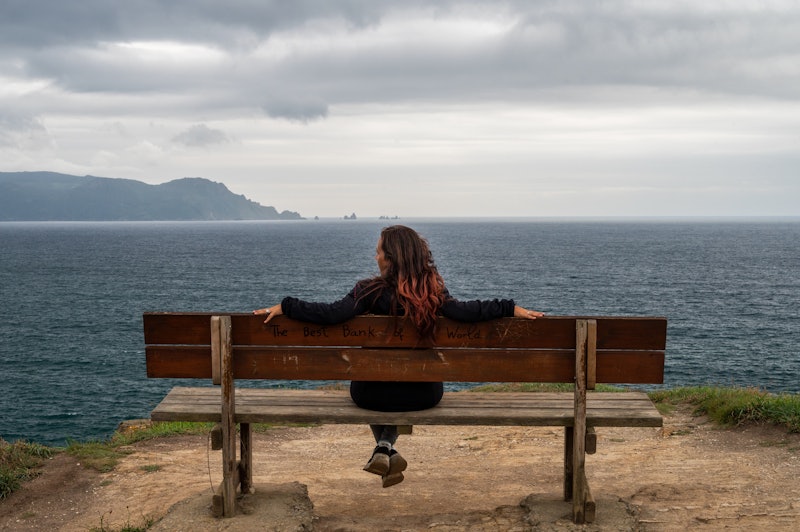 ORTIGUEIRA, GALICIA, SPAIN - 2021/07/13: A woman sits on a bench overlooking the Atlantic on the Loi...