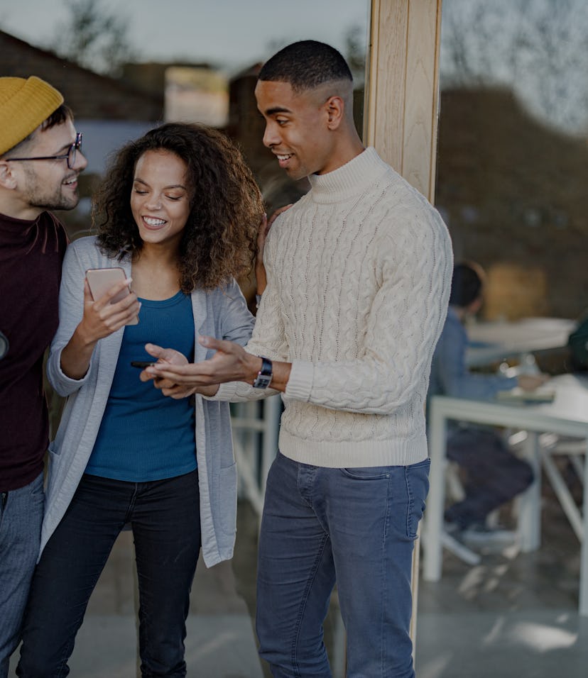 Happy university students communicating during a break in front of classroom. Focus is on woman usin...