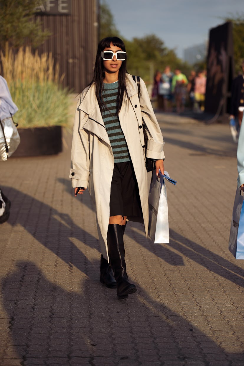 COPENHAGEN, DENMARK - AUGUST 12: Guest wearing black skirt, long boots and beige coat outside Rotate...