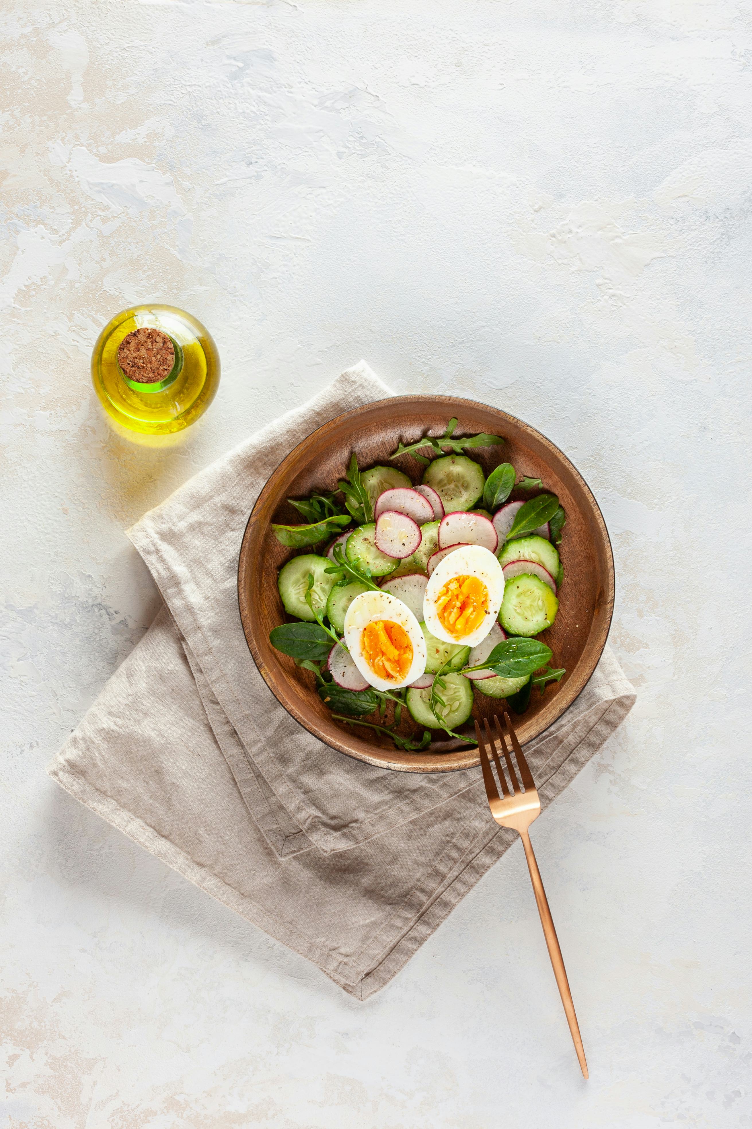 salad of radish, cucumber, arugula and boiled egg with olive oil in a wooden bowl