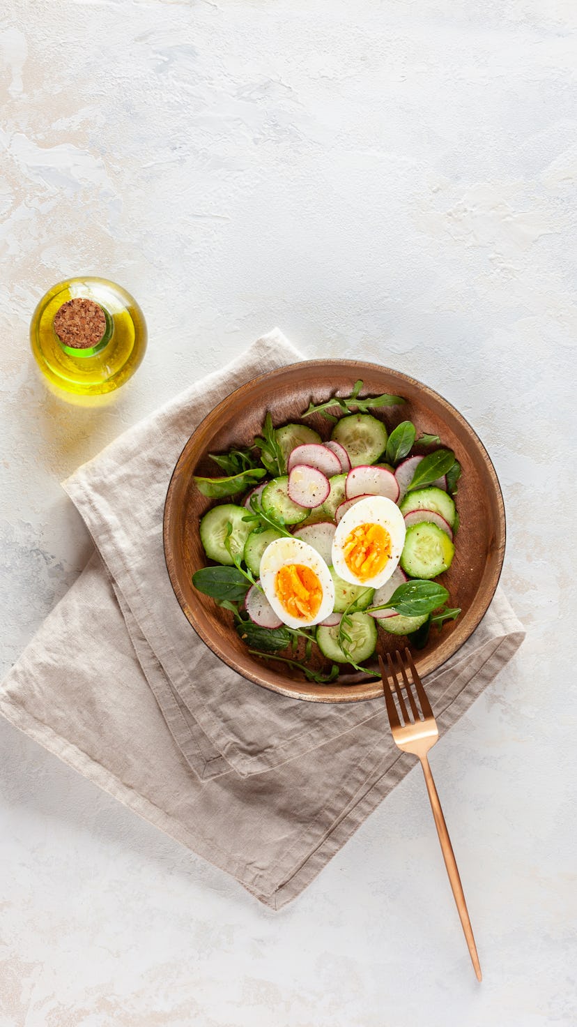 salad of radish, cucumber, arugula and boiled egg with olive oil in a wooden bowl