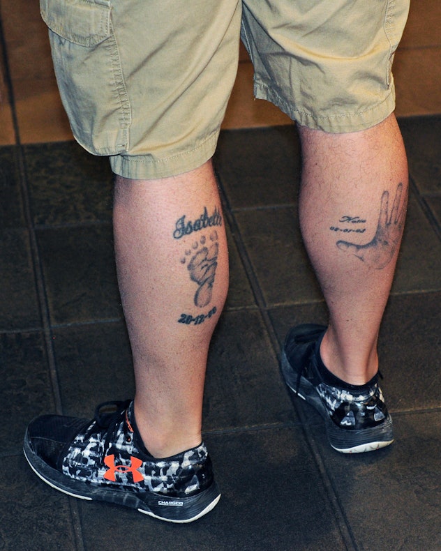   A man wearing cut off cargo pants sports tattoos on his calves based on his childrens' footprint a...