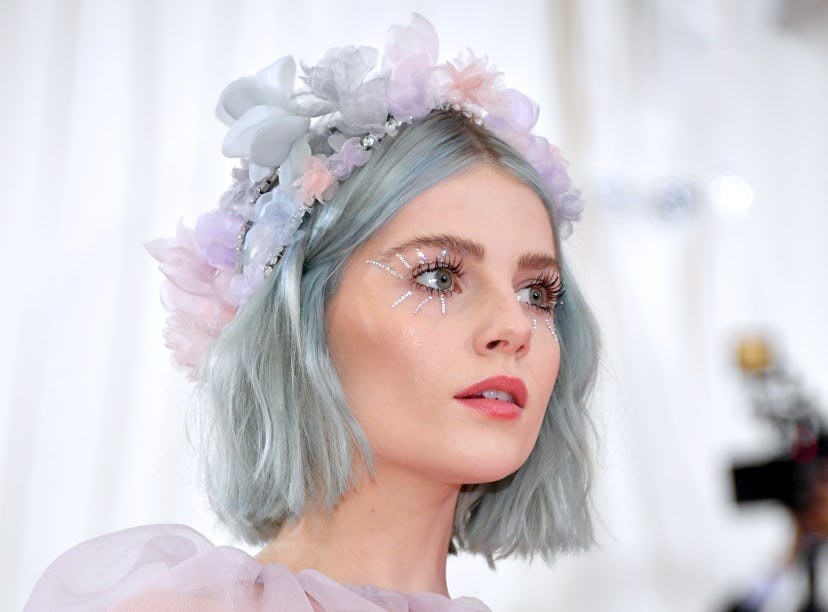 Lucy Boynton wears a flower crown and pastel hair and eye makeup with small rhinestone starbursts co...