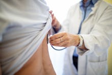 Cropped of female doctor examining patient. Medical professional checking woman's back with stethosc...