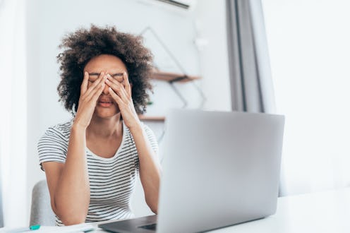 A person covers their face with their hands while working from home on their laptop. A good night's ...