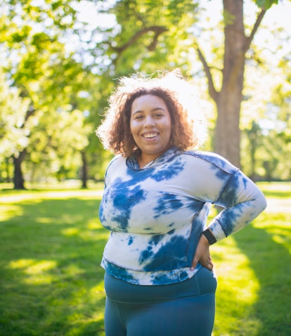 A plus-size Black woman with short curly hair looks radiant while standing in the sun