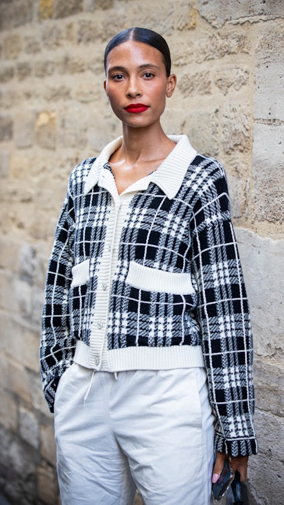 PARIS, FRANCE - SEPTEMBER 30: A guest, wearing a black and white checked cardigan and white pants, i...