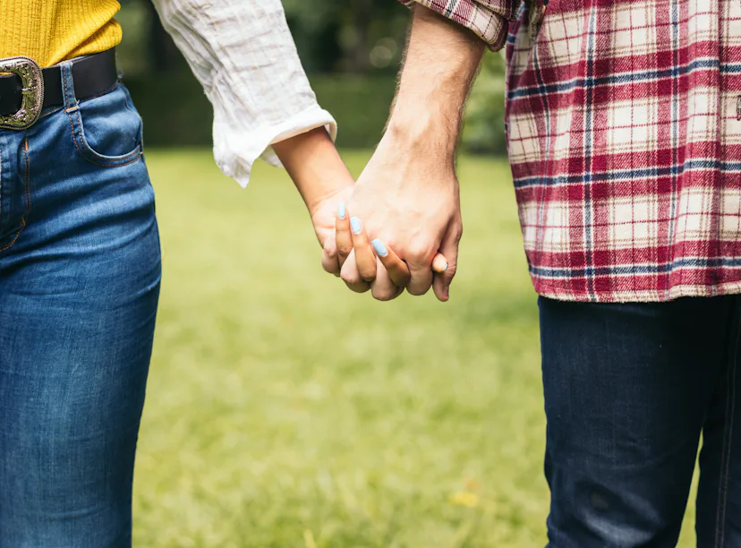 Anonymous man and woman holding hands while standing on grassy lawn on summer date in park