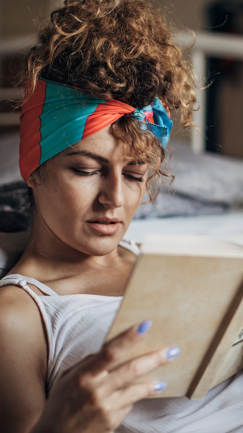 One woman sitting on the floor in bedroom at home. She is reading a book.