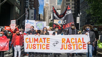 Environmental justice activists march in the street carrying a "Climate Justice [is] Racial Justice"...
