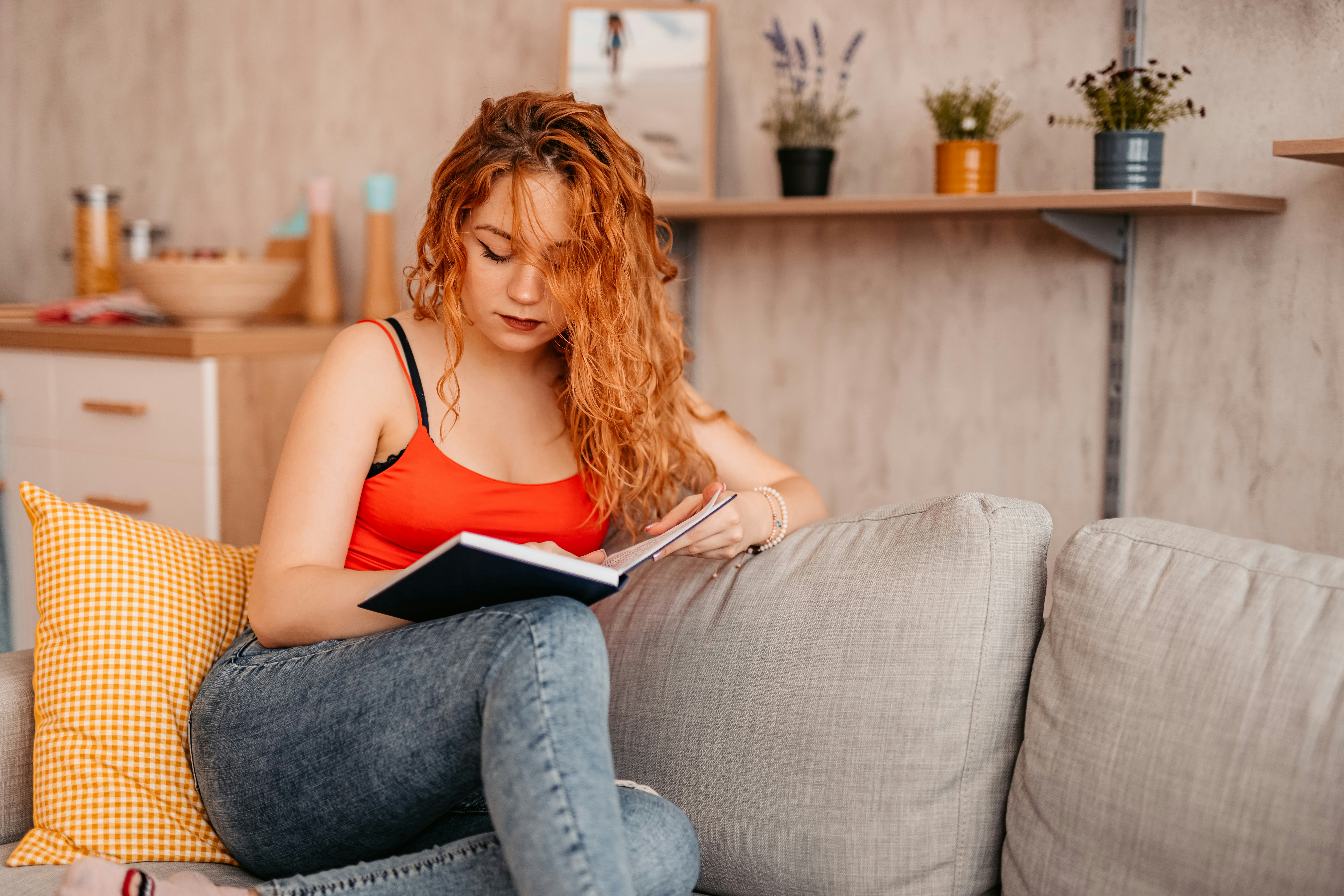 Beautiful young woman At Home sitting On Sofa and Reading Book.