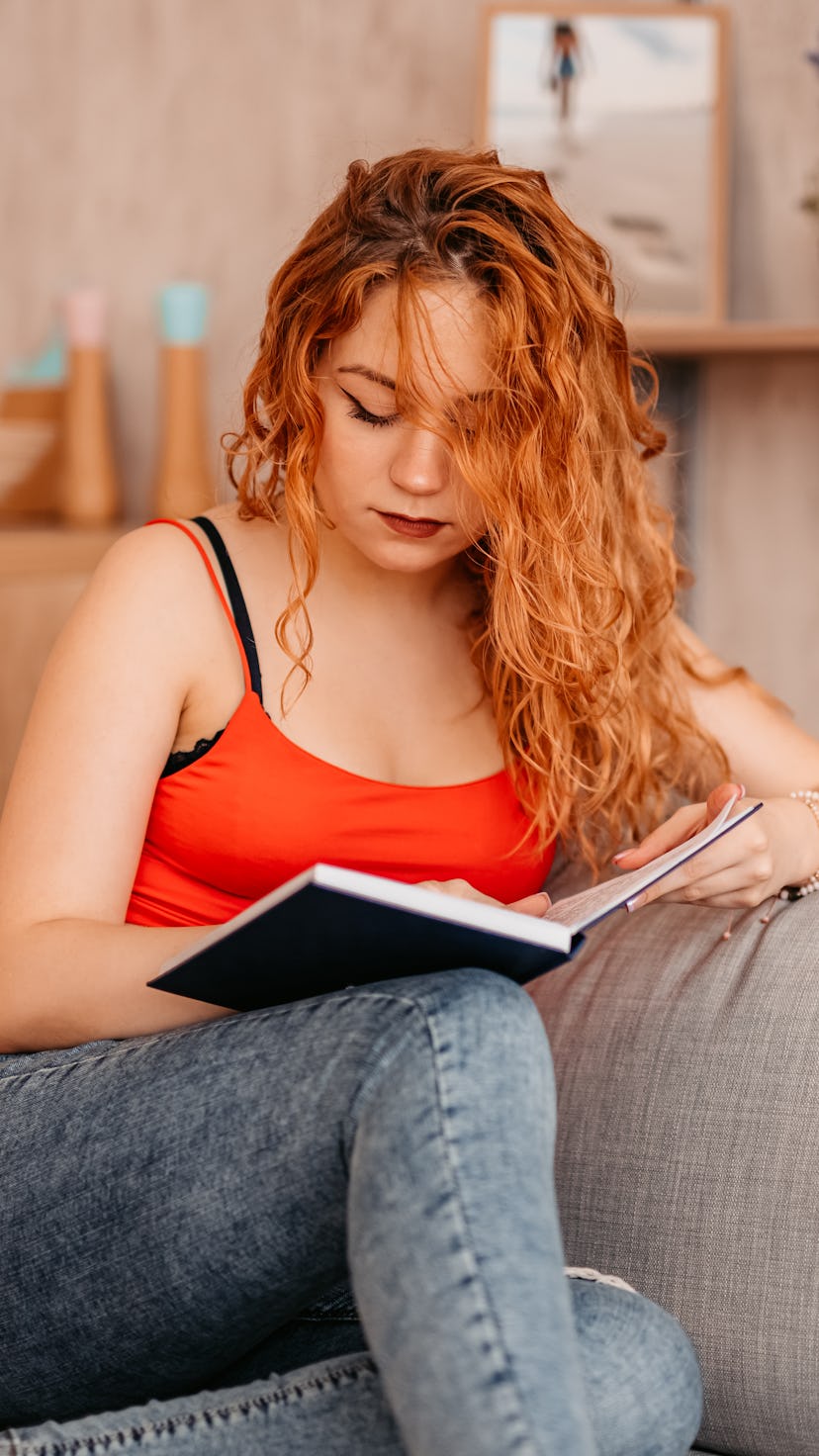Beautiful young woman At Home sitting On Sofa and Reading Book.