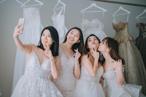 happy playful asian chinese bride and bridesmaid taking selfie with smart phone with joy at bridal s...