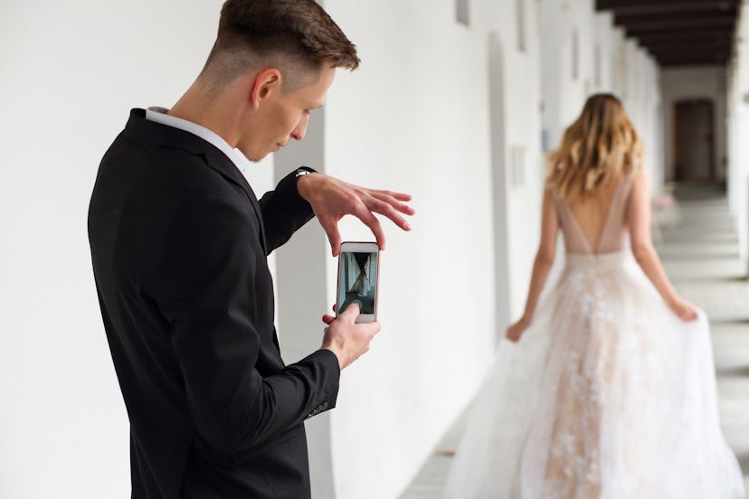 Man and woman in formal dresses. Man photographing his new wife. White columns in the background.