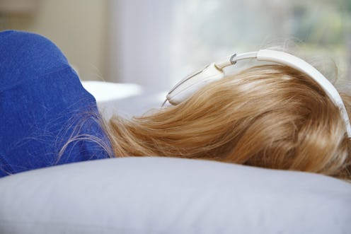 Blond woman lying on a bed and wearing headphones while listening music