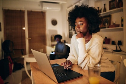 Beautiful African American woman studying in the living room on a laptop computer while living with ...