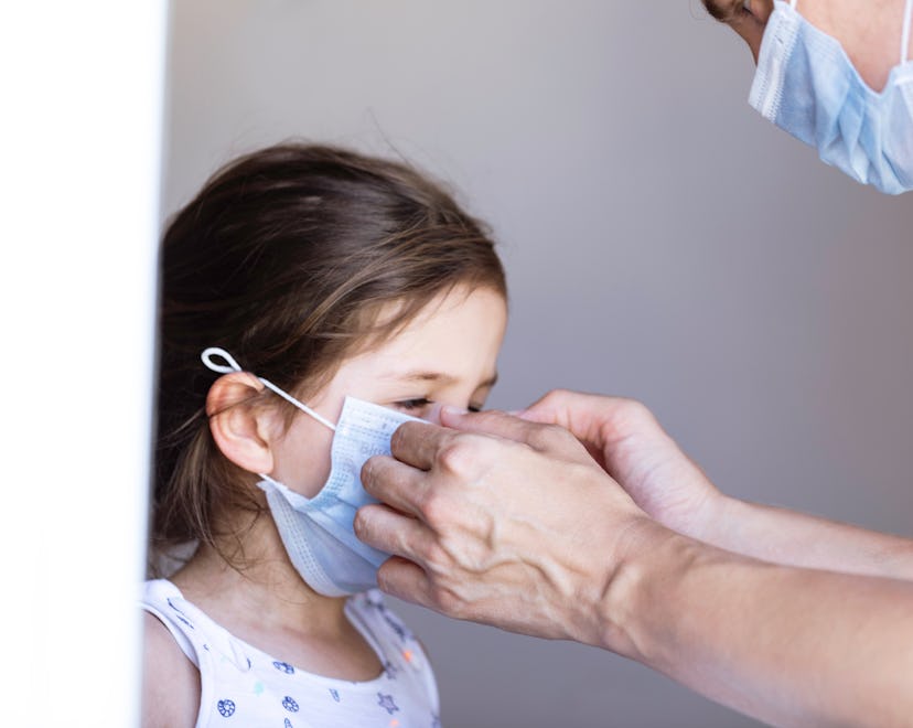 Mother of a caucasian little girl is correcting her daughters  protective face mask .