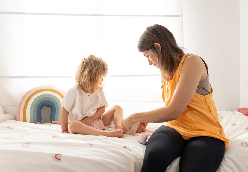 Mother helping to put on her little daughter's shoes. Caucasian 3 year old girl getting dressed with...